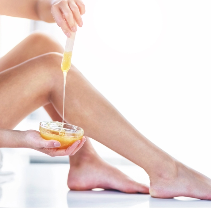 Woman applying hot wax to her legs in a bathroom.